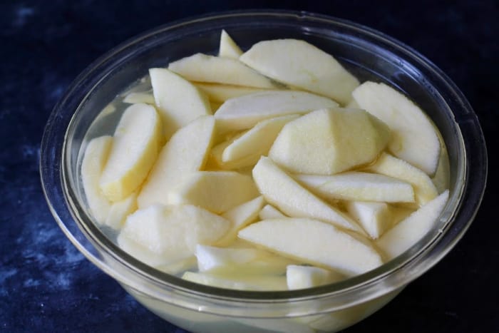 Peeled, sliced apples soaking in a bowl of lemon juice and water to prevent them from turning brown once frozen. 