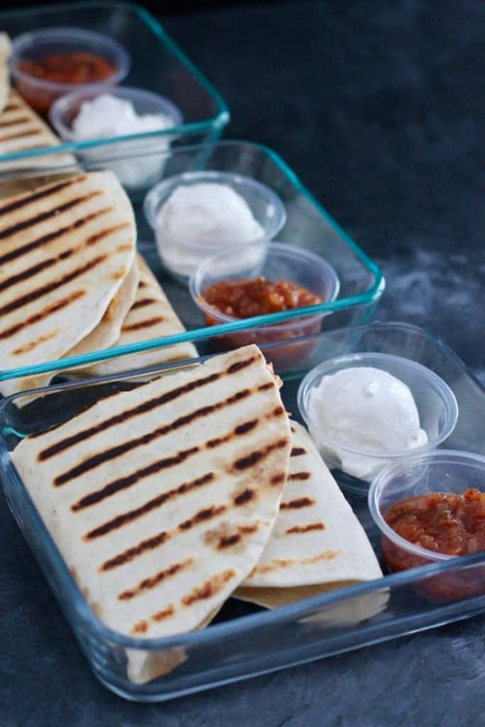 Grilled quesadillas in to-go glass container with side of salsa and sour cream.