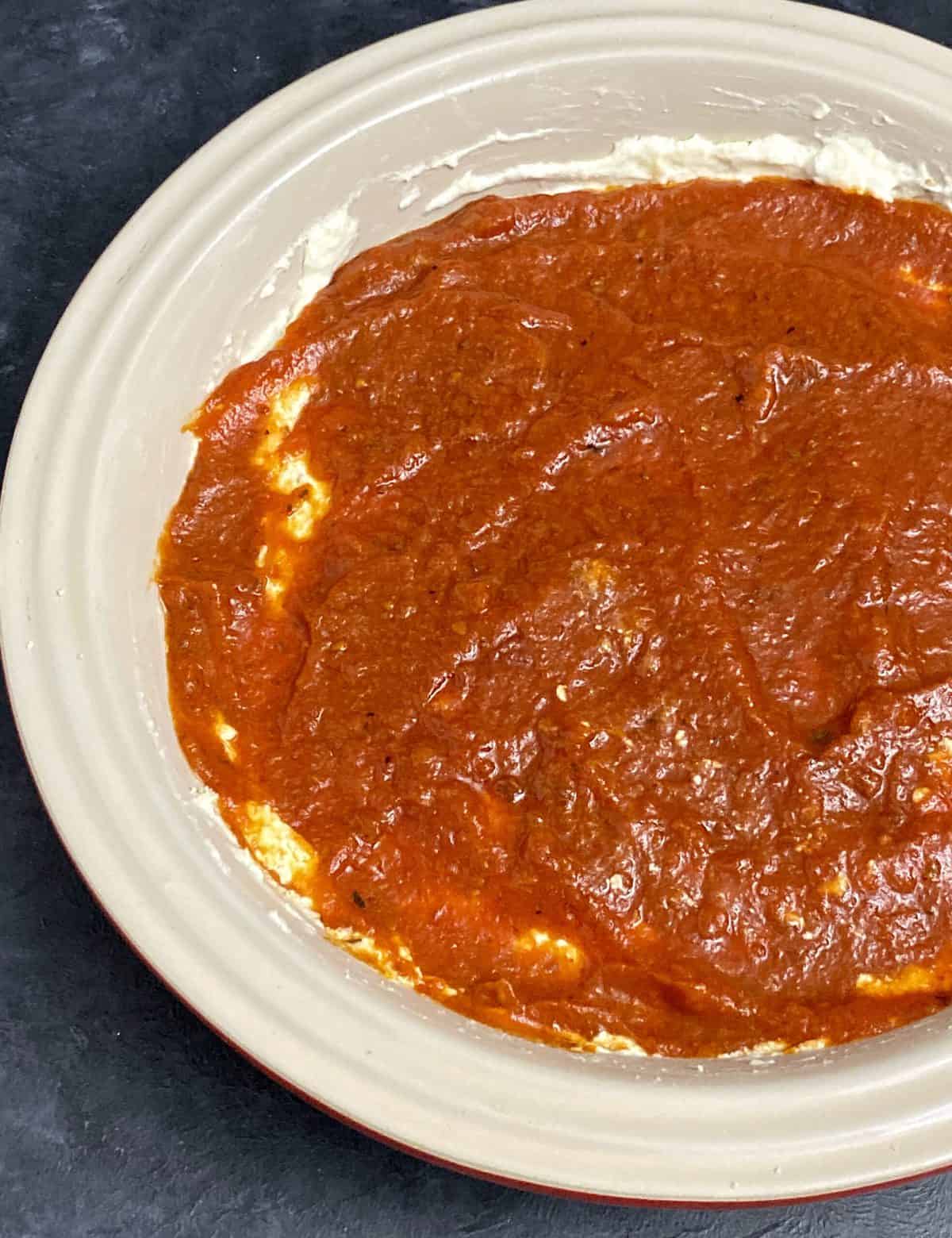 Layers of cream cheese covered in tomato sauce in a baking dish.