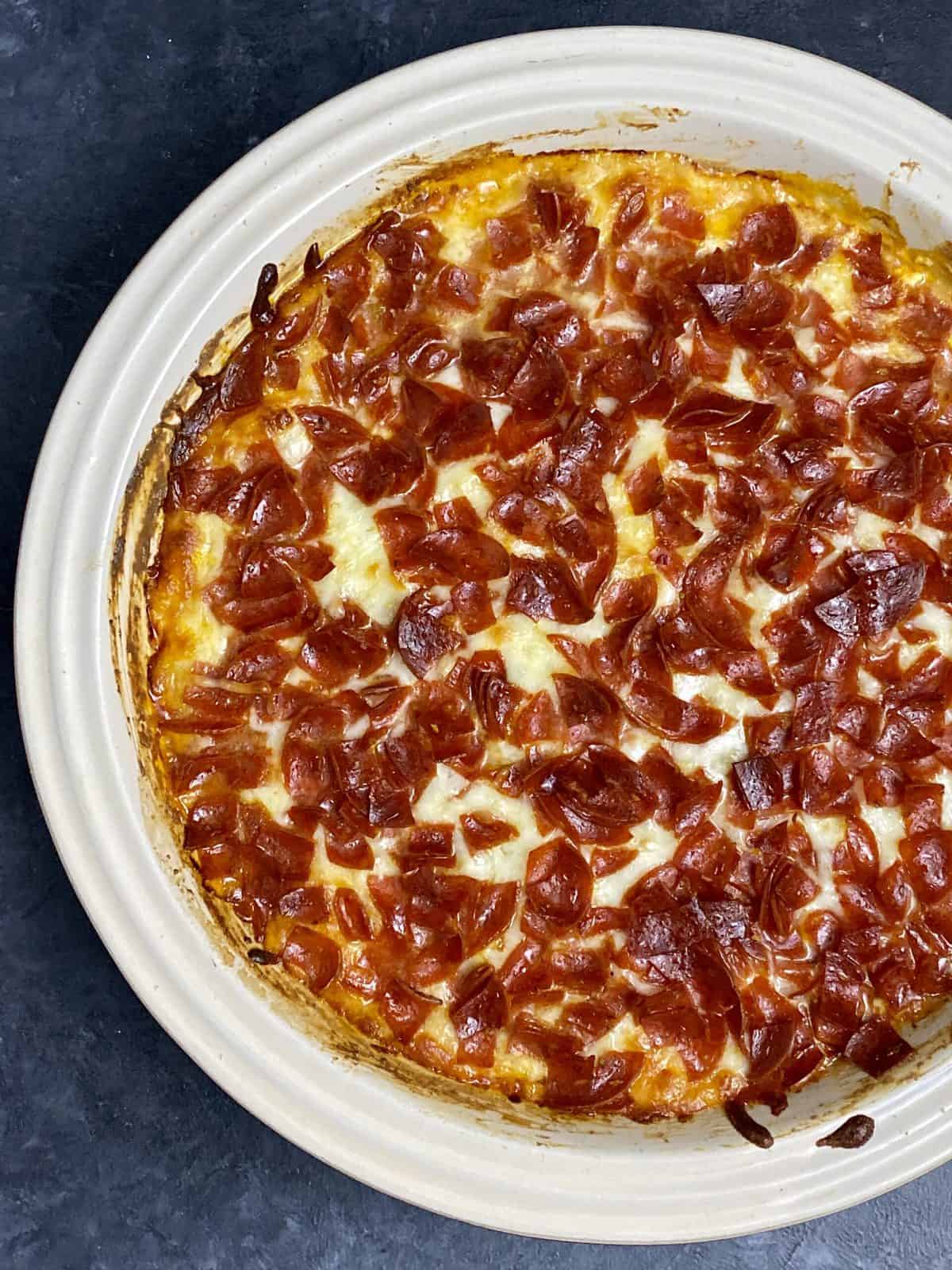 Baked pizza dip with charred edges and bits of pepperoni on top of a cheesy base.