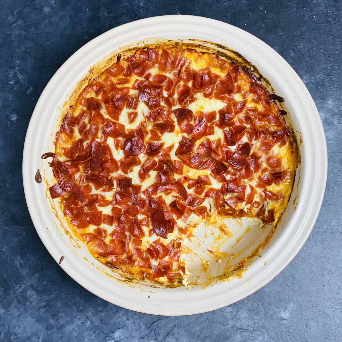 Baked pizza dip recipe with a chunk missing that's been spooned out.