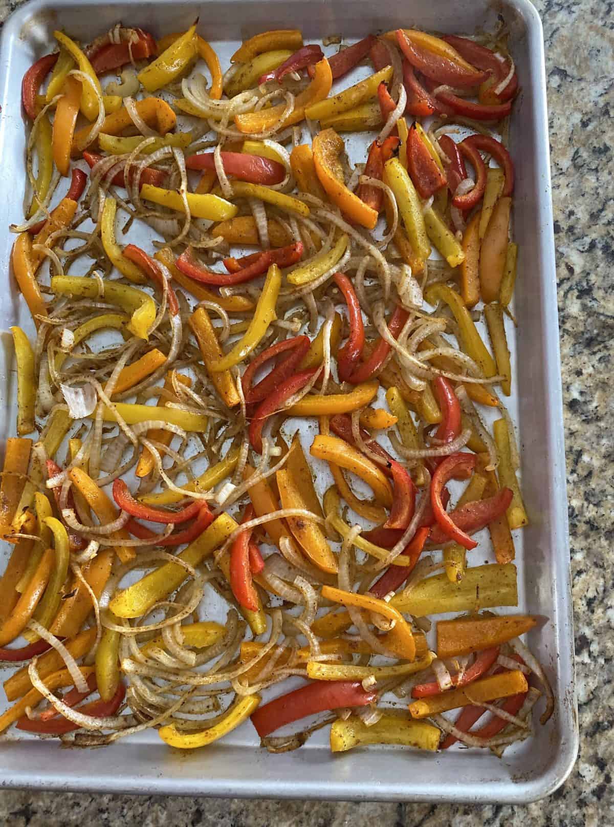 Roasted onions and peppers on a sheet pan in preparation for a sheet pan fajita dinner.