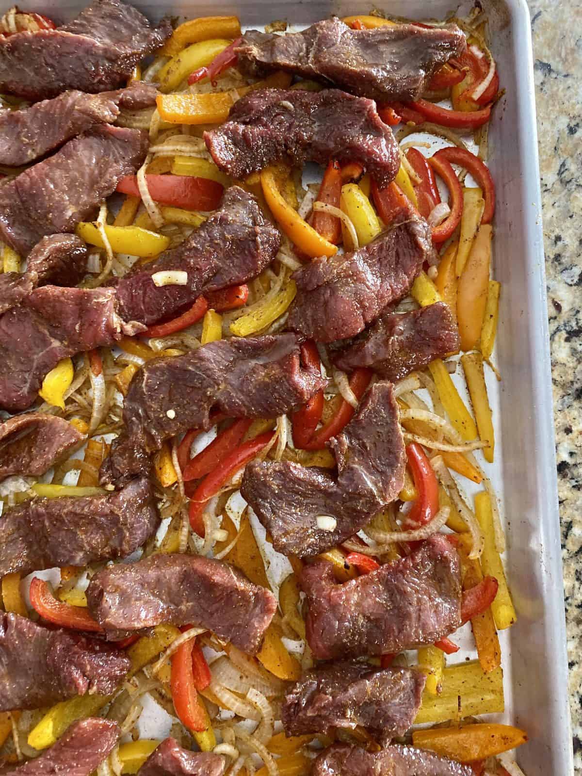 Close up of steak, onions and bell peppers sliced and cooked on a sheet pan. 