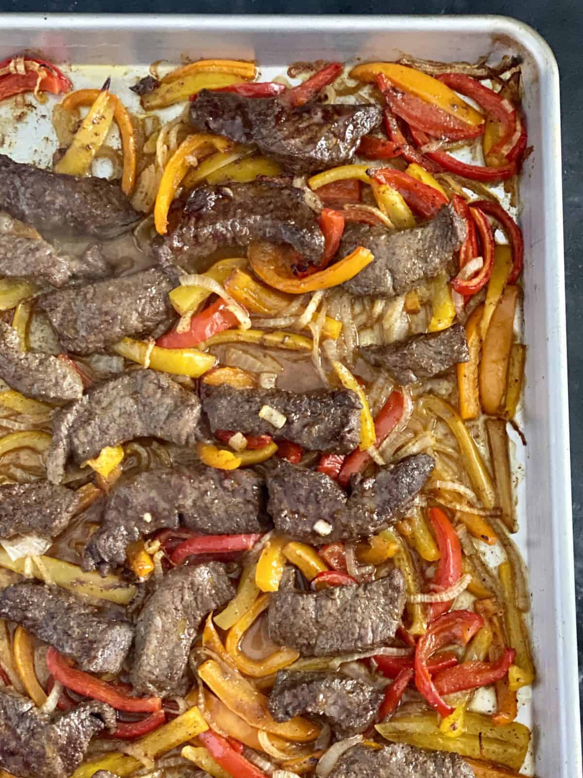 Slightly charred veggie and steak sheet pan fajitas on a sheet tray. 