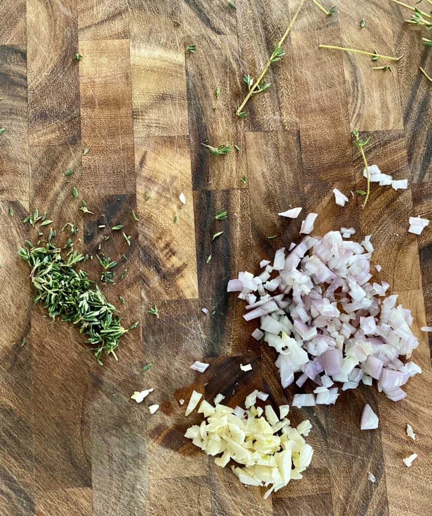 Chopped thyme, shallots, and garlic on a wooden cutting board.