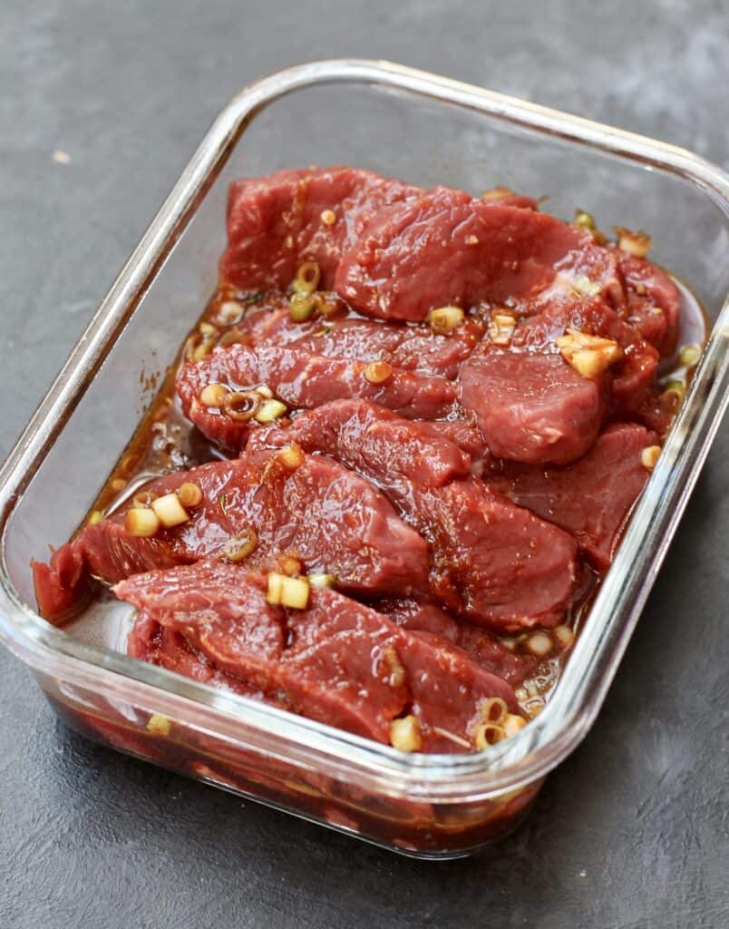 Strips of sirloin steak marinating in a glass container