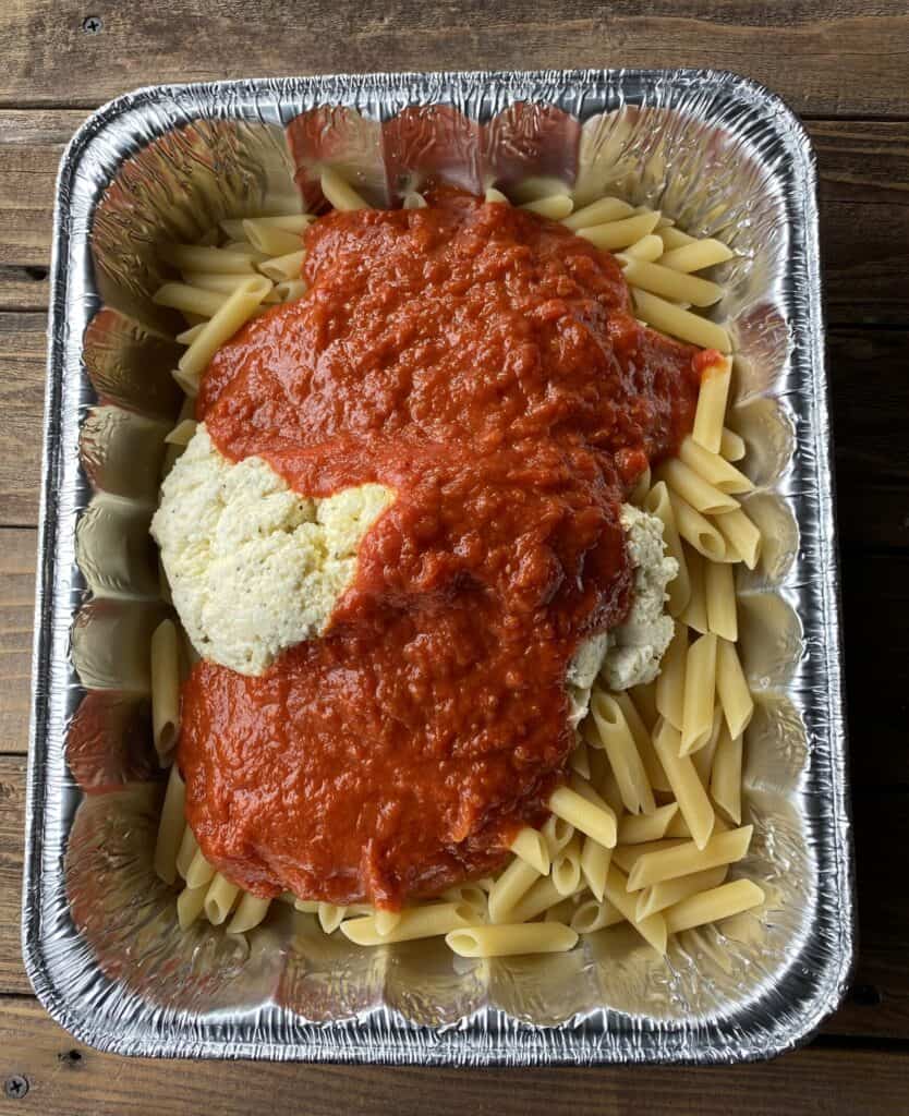 Disposable aluminum baking dish filled with pasta, ricotta cheese and tomato sauce