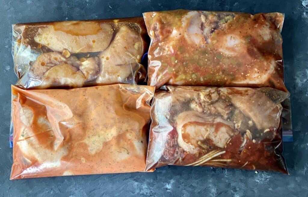 Four different chicken breast recipes with marinade in ziploc bags prior to freezing.