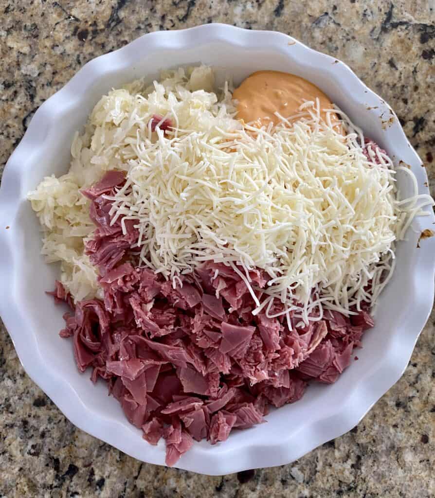 Ingredients for a rueben dip prior to baking such as corned beef, cheese, thousand island and sauerkraut 