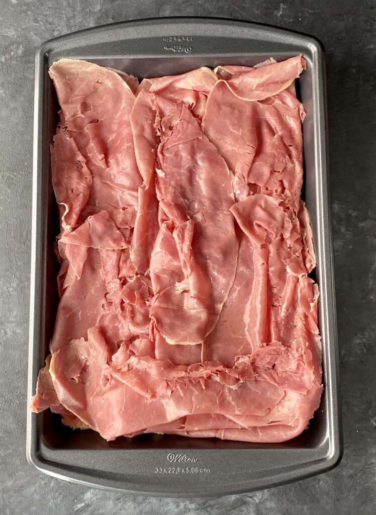 Tray of corned beef on top of rolls. 