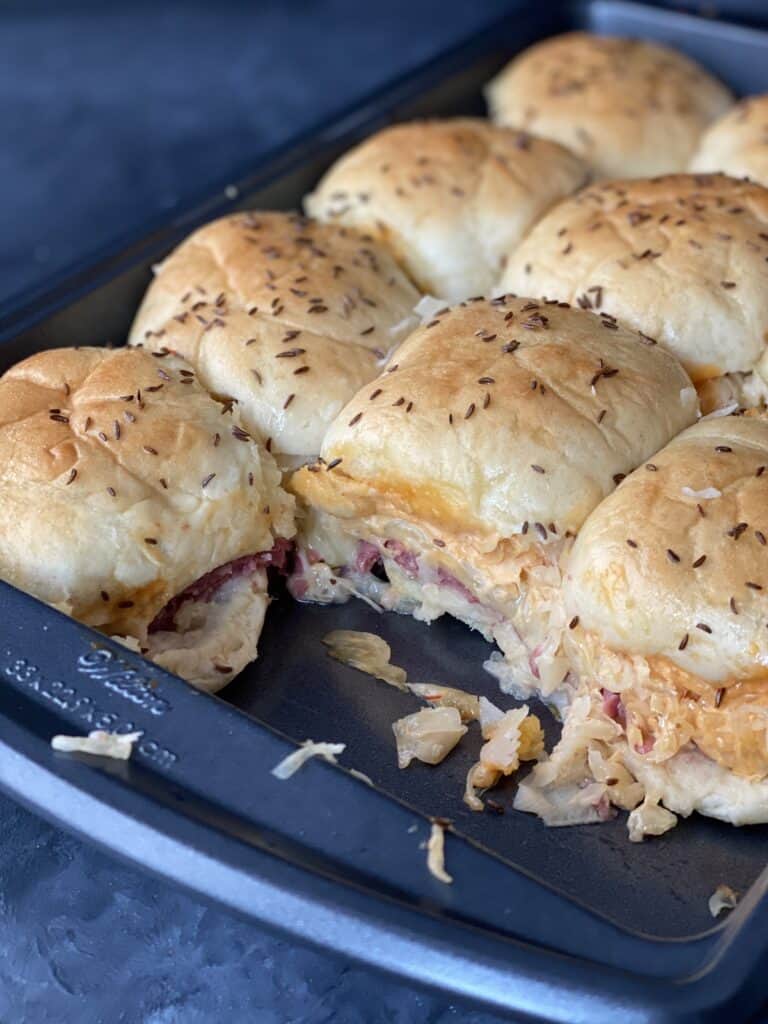 Baked reuben sliders with layers of corned beef, sauerkraut, russian dressing and swiss cheese.