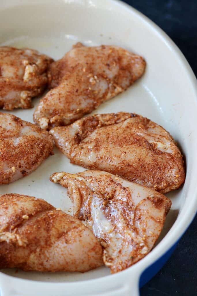 Raw chicken covered in a seasoning mixture in a white bowl