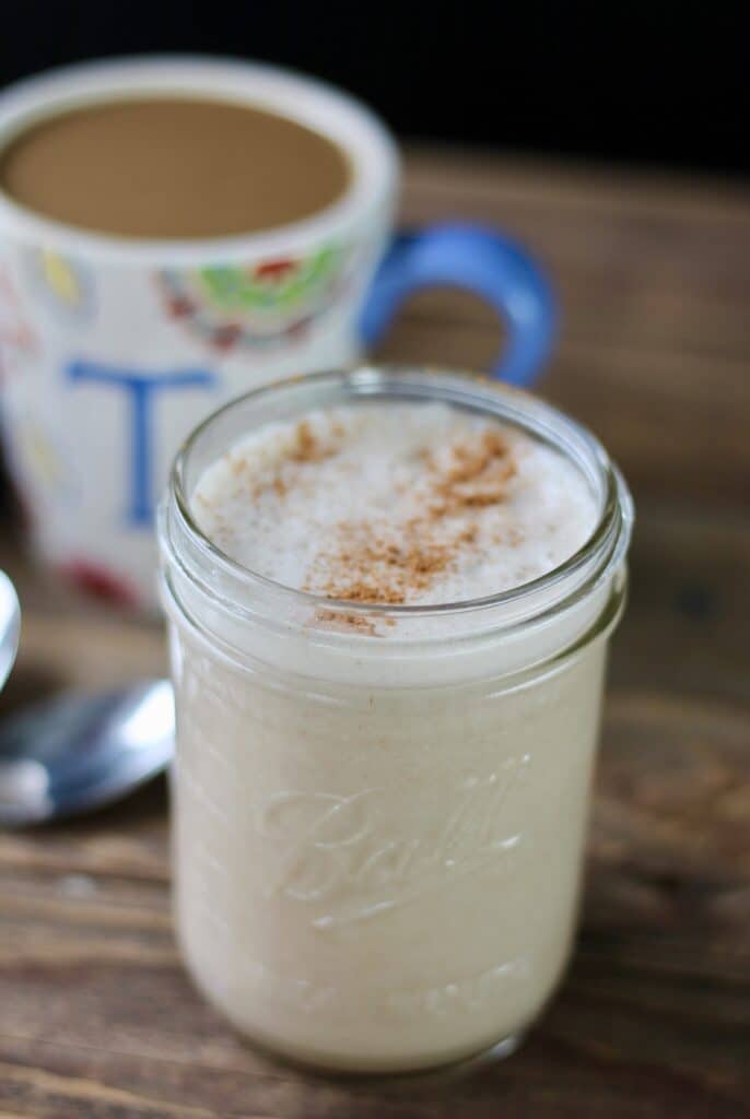 Mason jar of homemade coffee creamer with a cup of coffee in the background.