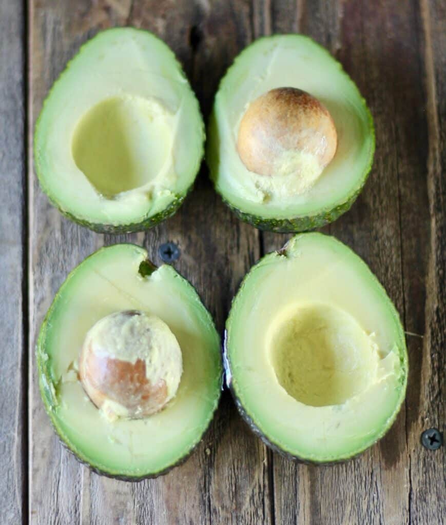 four avocado halves on a wooden table