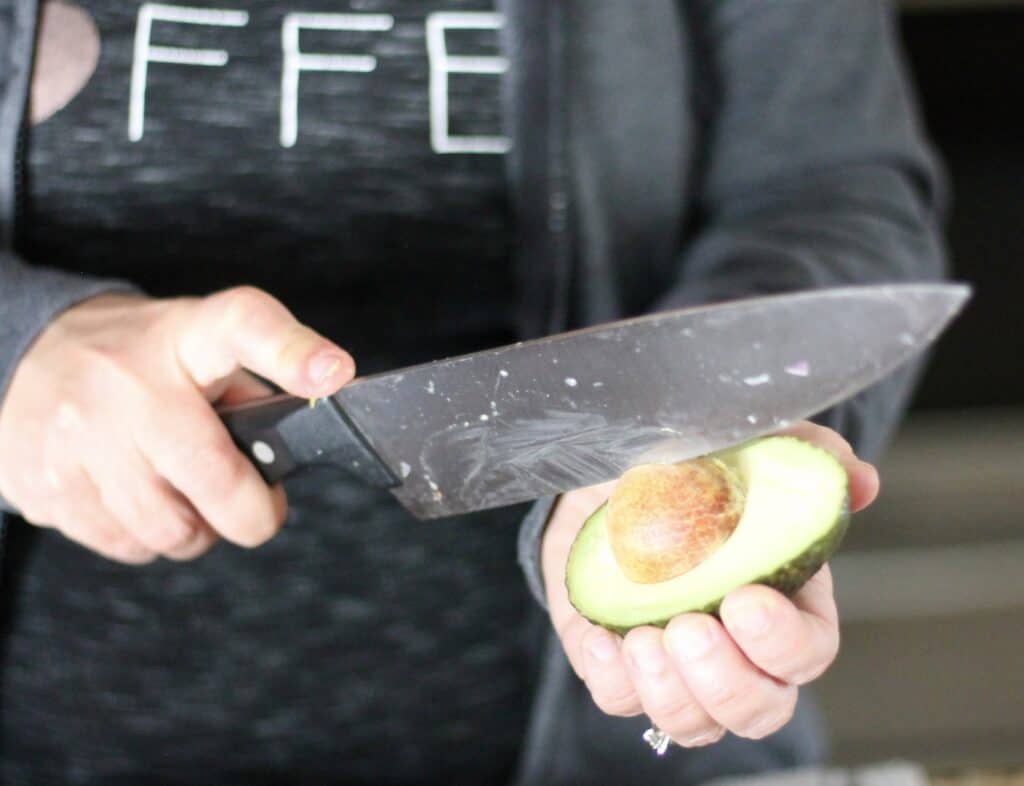 Woman demonstrating how to remove an avocado pit with a knife