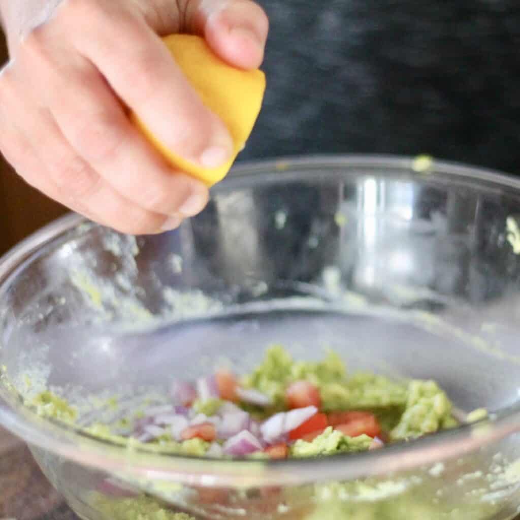 Woman squeezing lemon into a bowl of avocado, tomatoes and onions.