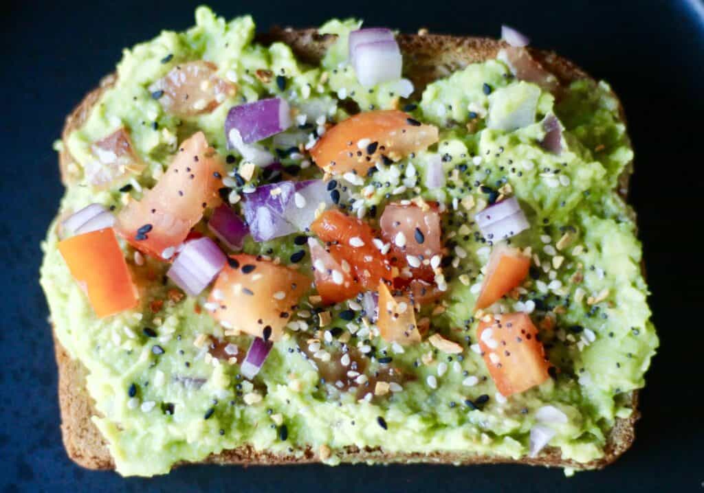 The best avocado toast, layered with mashed avocado, chunks of tomato and onion, and everything but the bagel seasoning