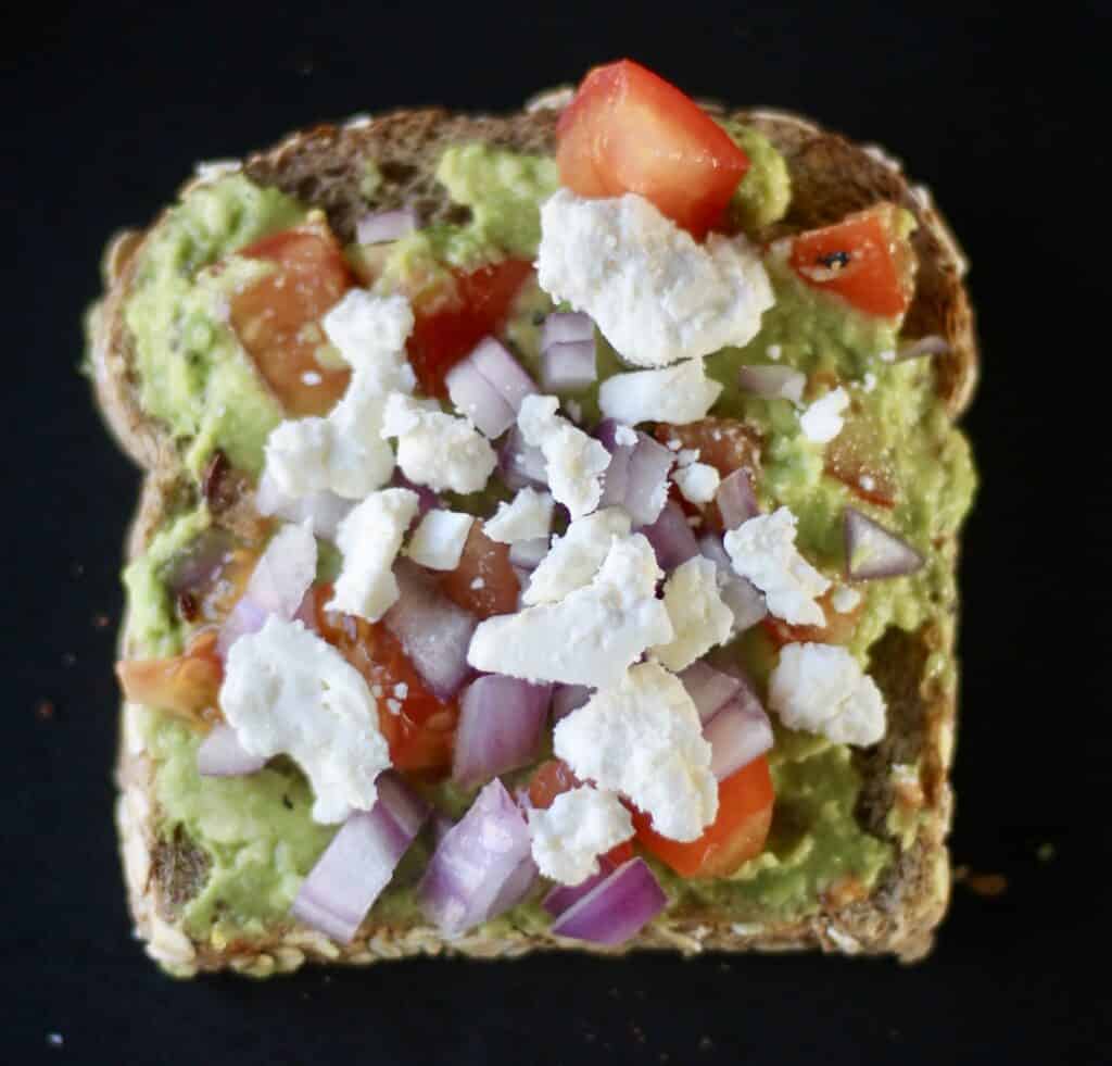 The best avocado toast - mashed avocado with chopped red tomatoes, onions, and feta