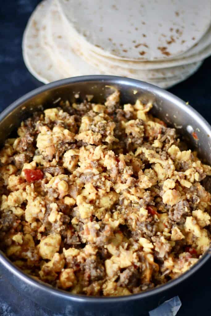 Large bowl of burrito filling with a stack of tortillas right next to it