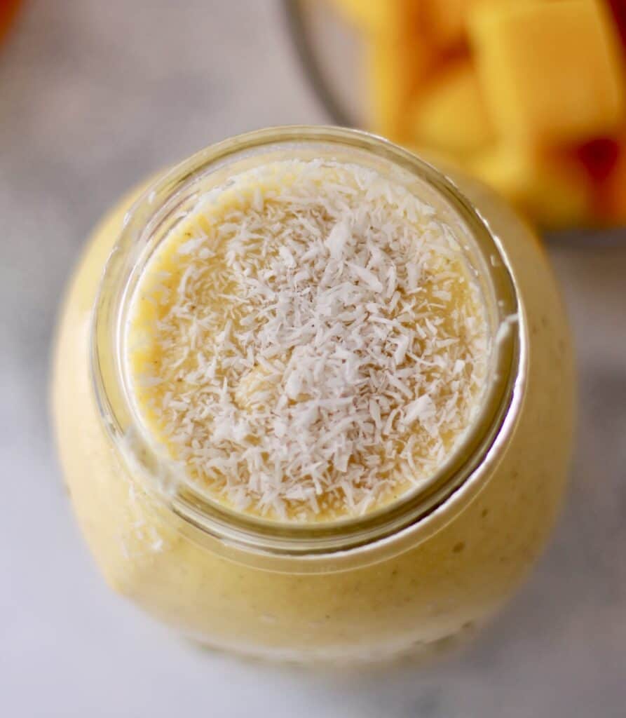 Mango smoothie in a mason jar topped with shredded coconut.