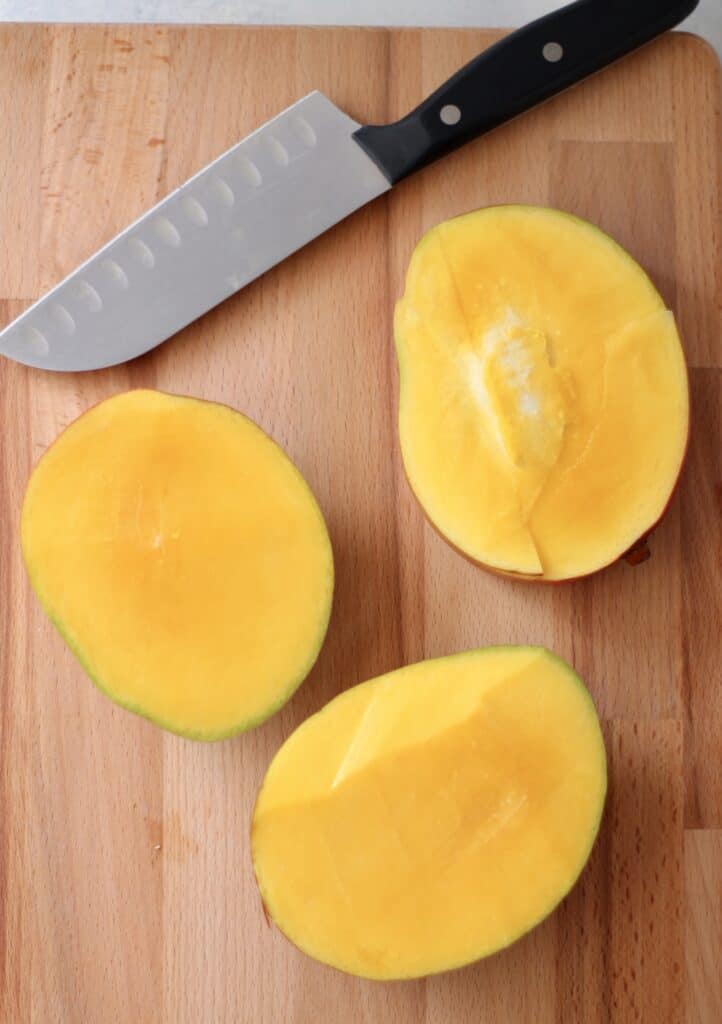 Mango sliced on a cutting board next to a knife. 