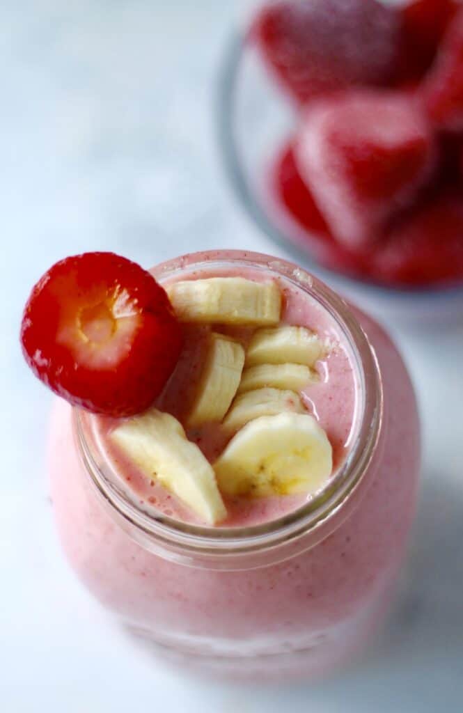 Mason jar filled with strawberry and banana smoothie with slices of fruit