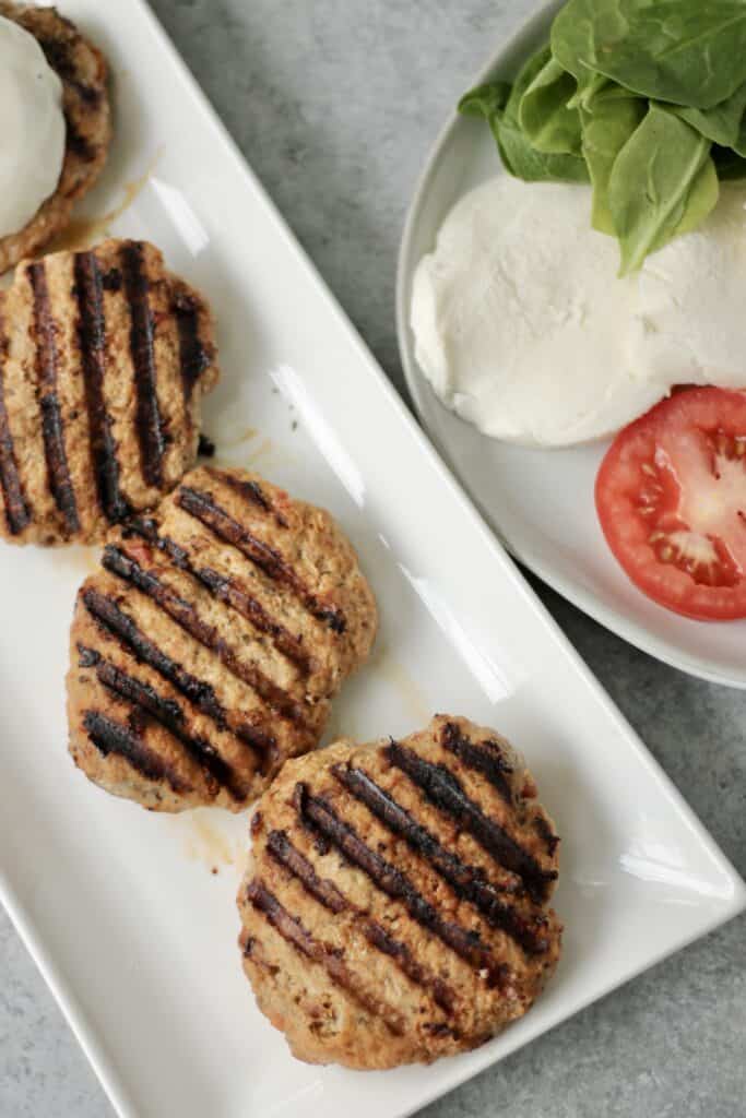 ground turkey burgers on a white plate next to a plate of mozzarella and tomatoes