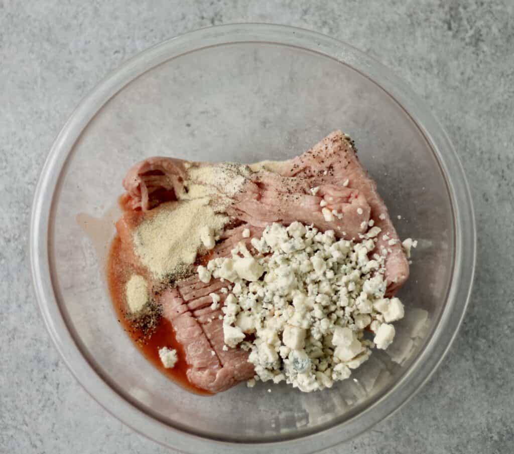 Ingredients for a buffalo turkey burget in a glass bowl - blue cheese, seasoning, ground turkey and hot sauce