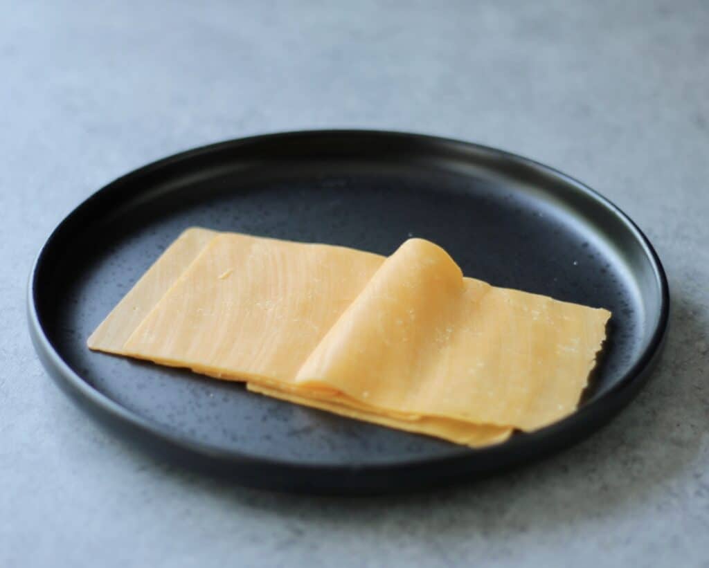 Thinly sliced cheddar cheese on a black plate