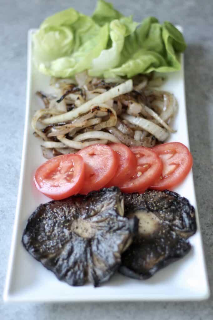 Plate of toppings for greek turkey burger - lettuce, onion, tomato, mushroom