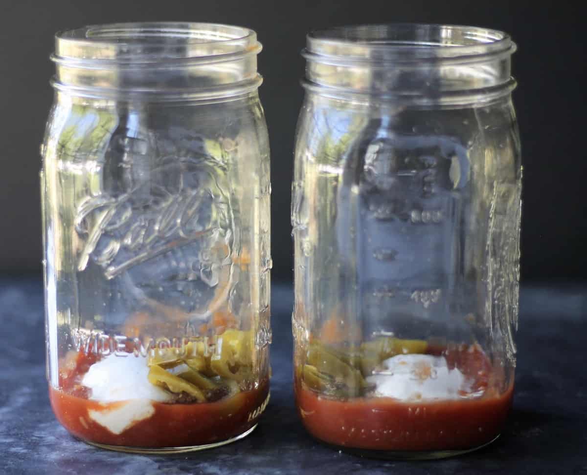 adding salsa, pickled jalapenos and vegan sour cream to mason jars 