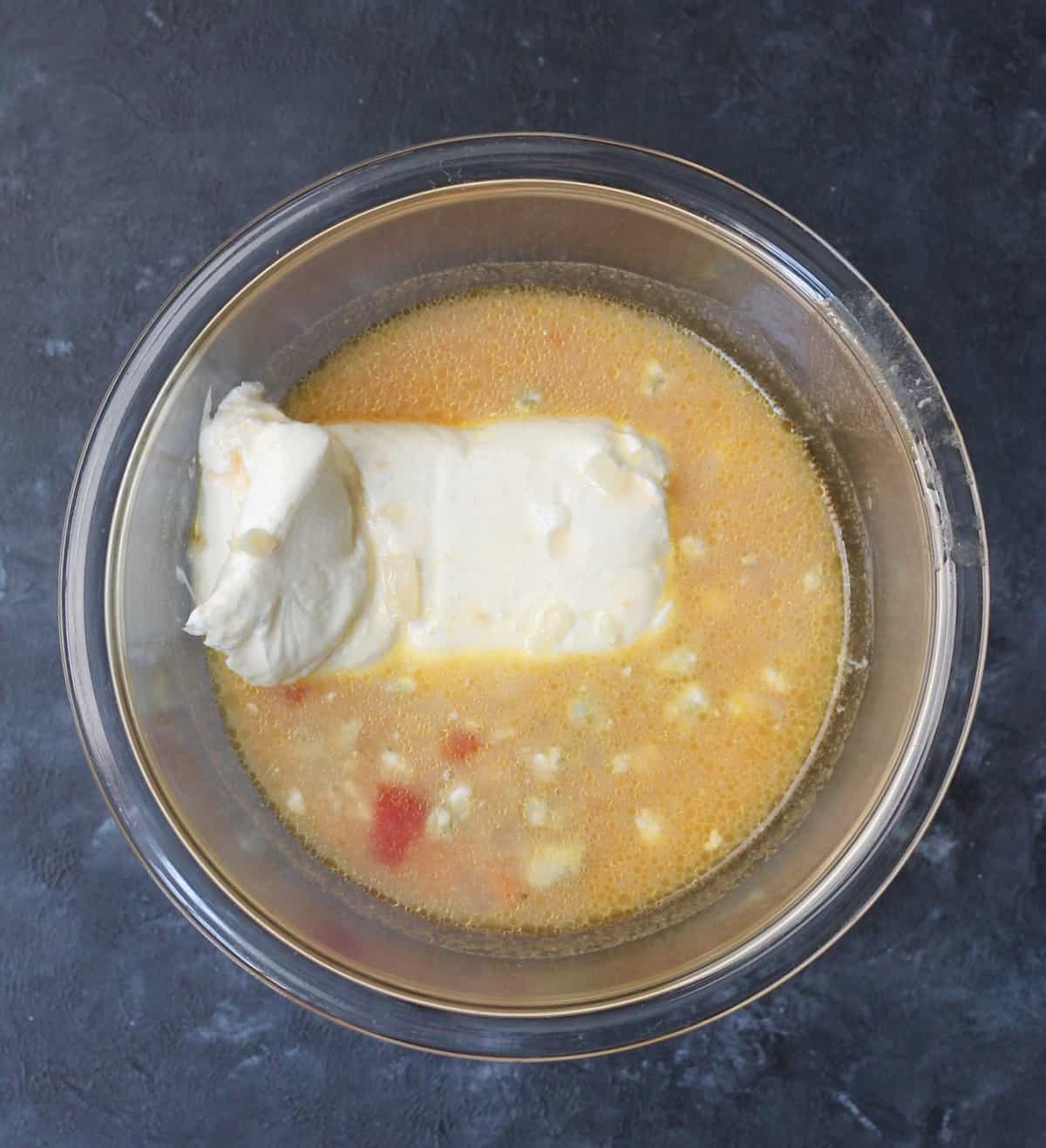 adding cream cheese with blue cheese crumbles and hot chicken broth to a glass bowl