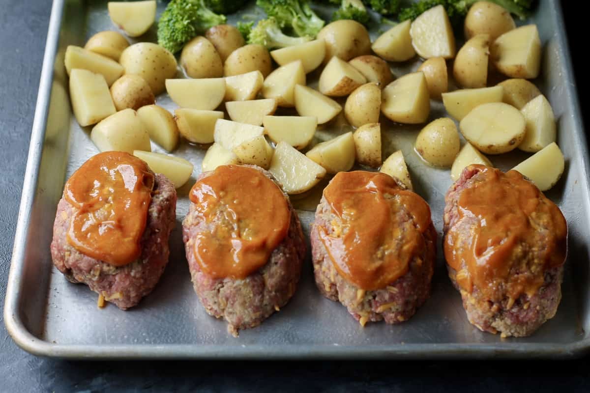 cooking mini meatloaves with potatoes and broccoli on a sheet pan