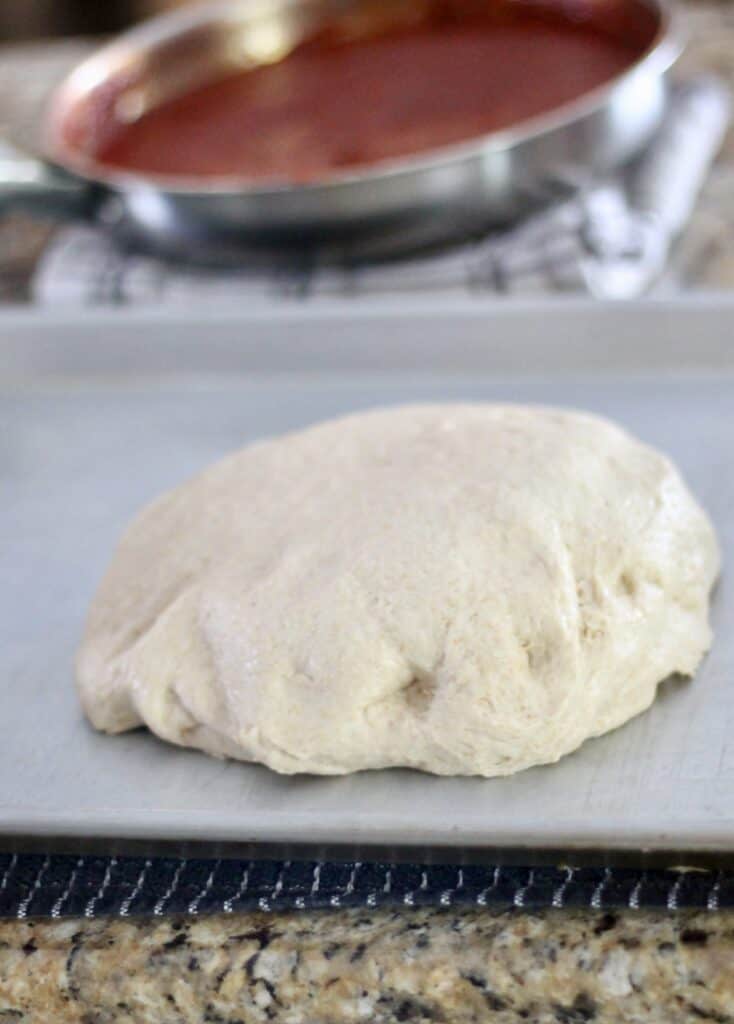 homemade pizza dough with pizza sauce in a pan in the background