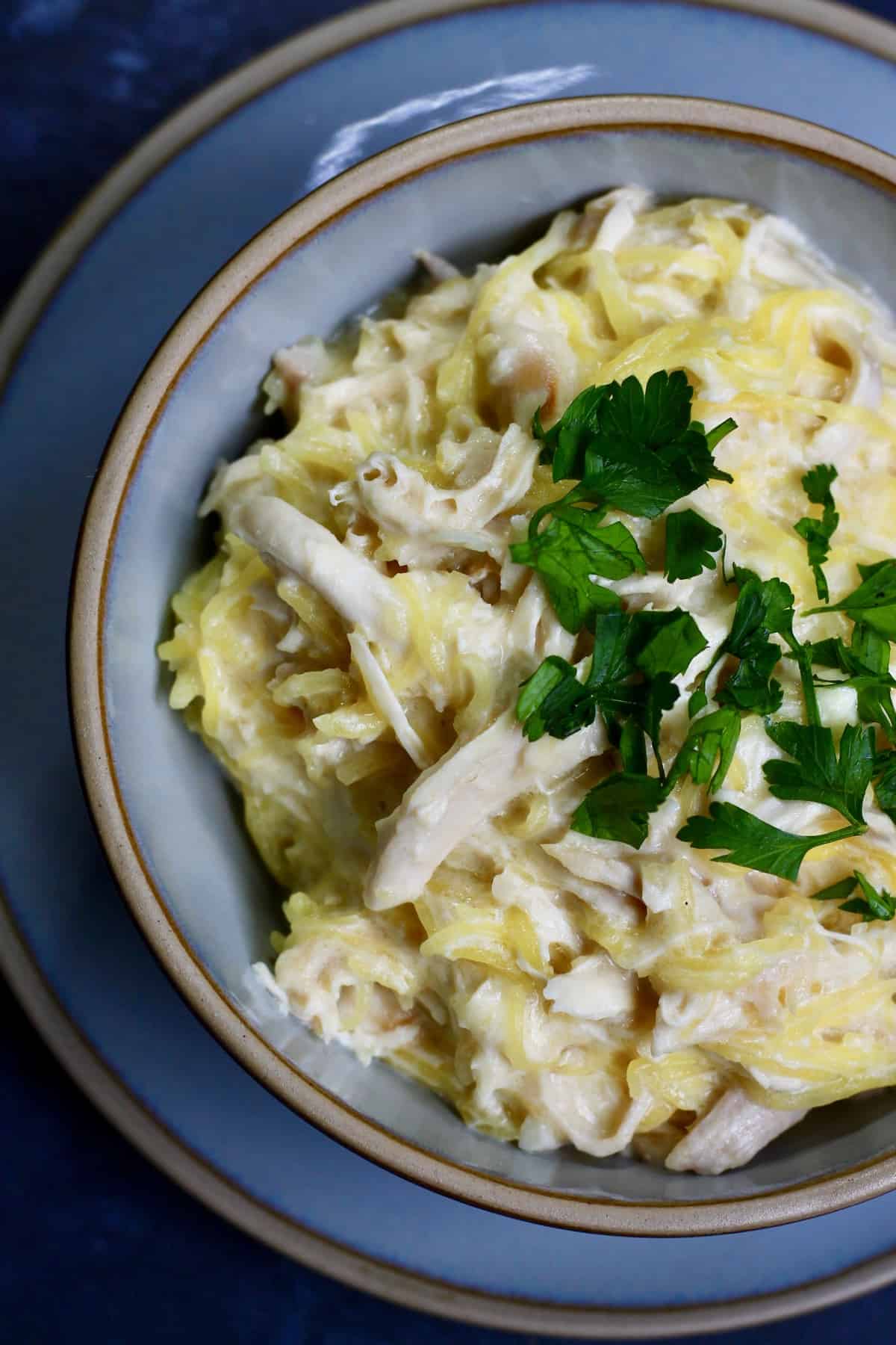 Spaghetti squash alfredo with chicken in a blue bowl and topped with parsley