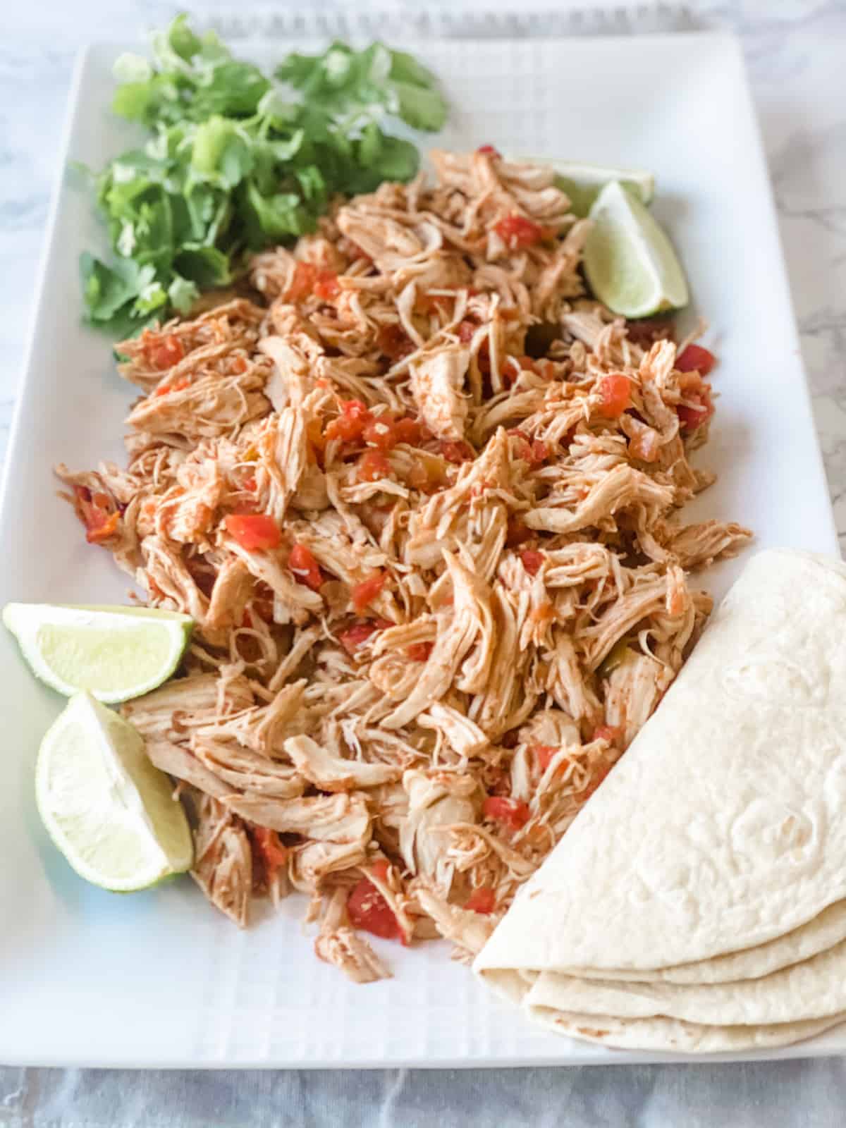 Slow cooker salsa chicken shredded on a platter with tortillas and lime
