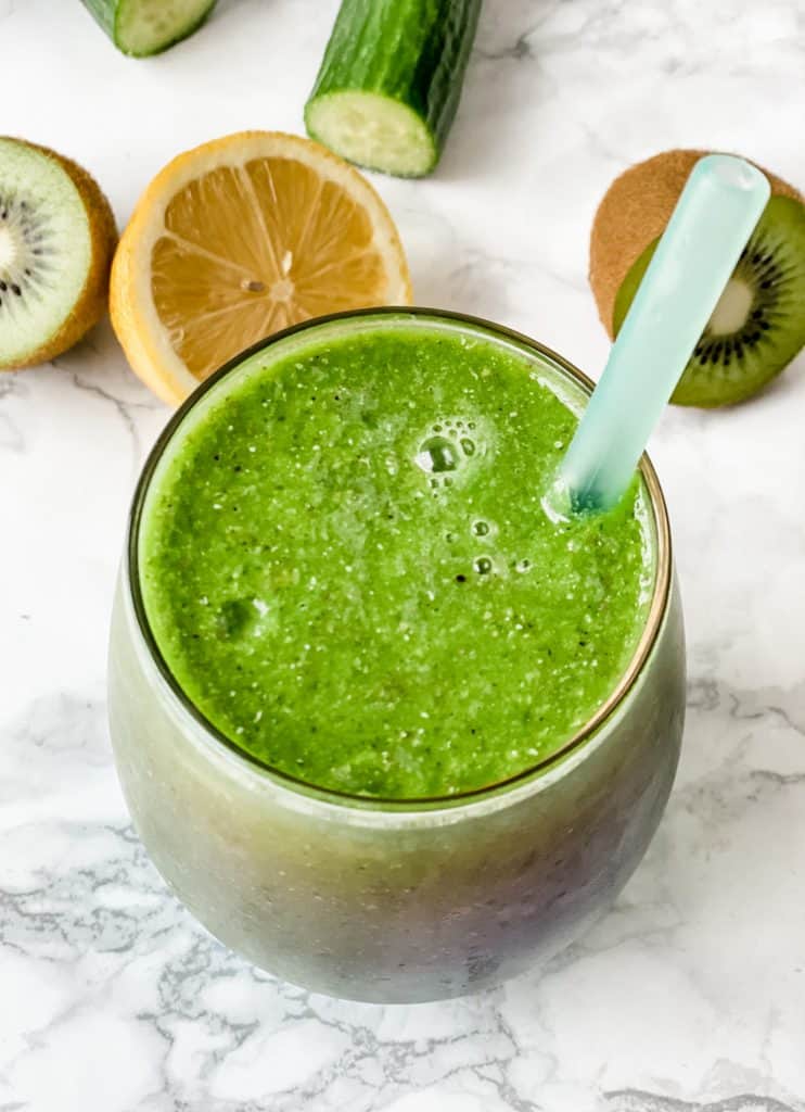 green smoothie with lemon, kiwi, and cucumber in the background.