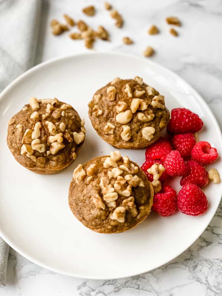 three banana nut muffins on a plate with raspberries