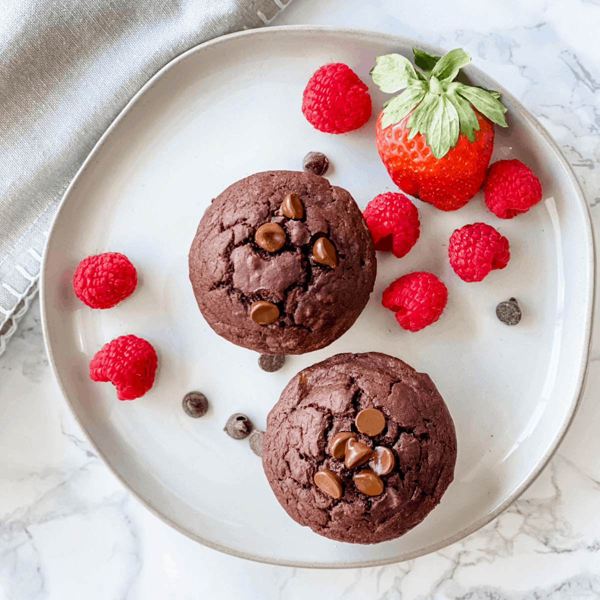 overhead picture of two banana muffins on a plate with strawberries and raspberries.