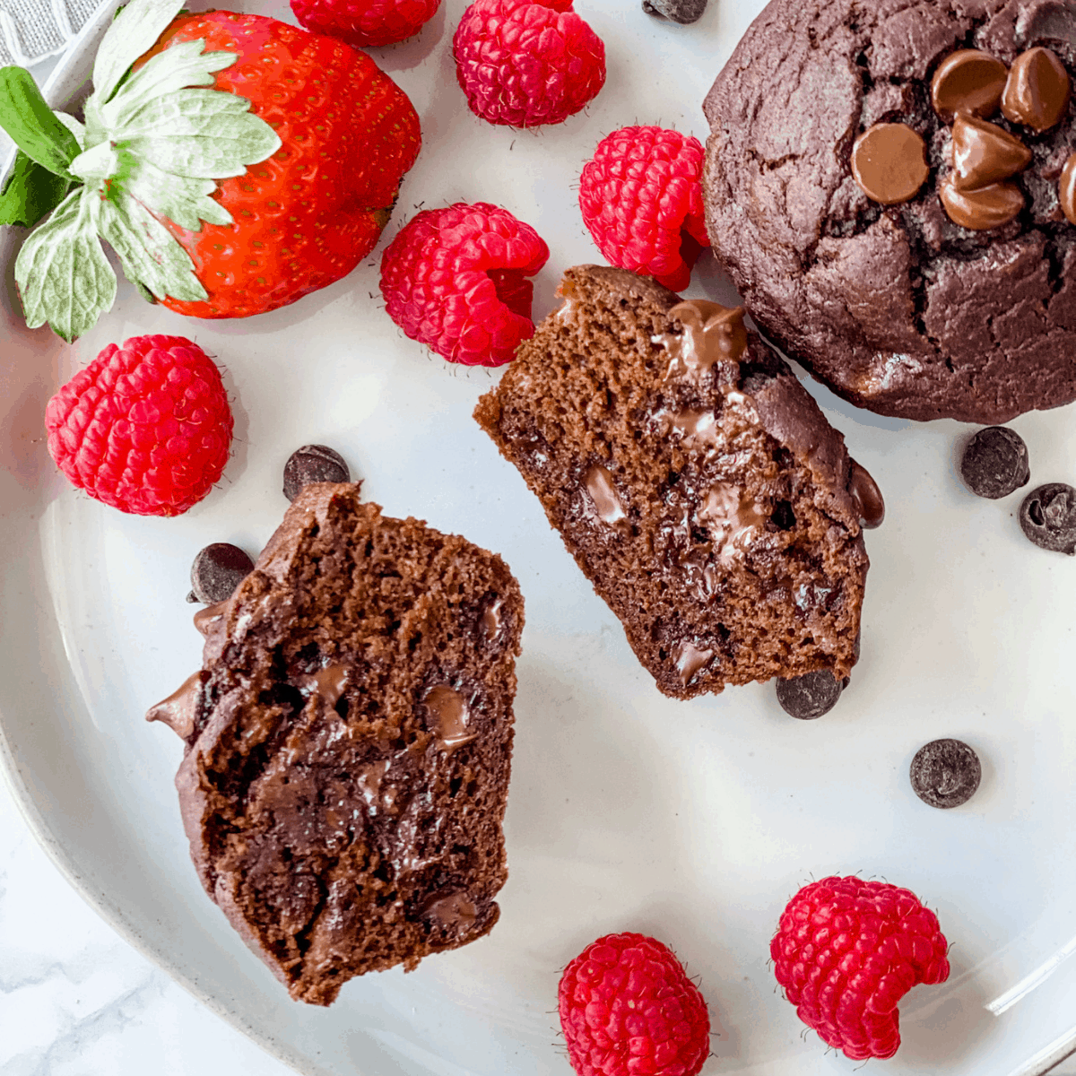 a chocolate banana muffin cut in half on a plate.