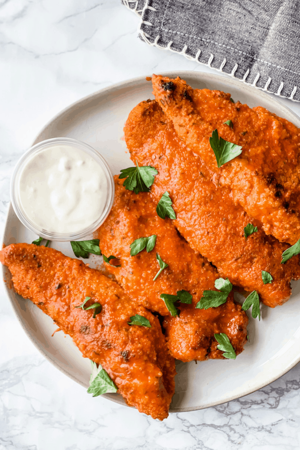 cooked buffalo chicken tenders on a plate with a side of blue cheese dressing.
