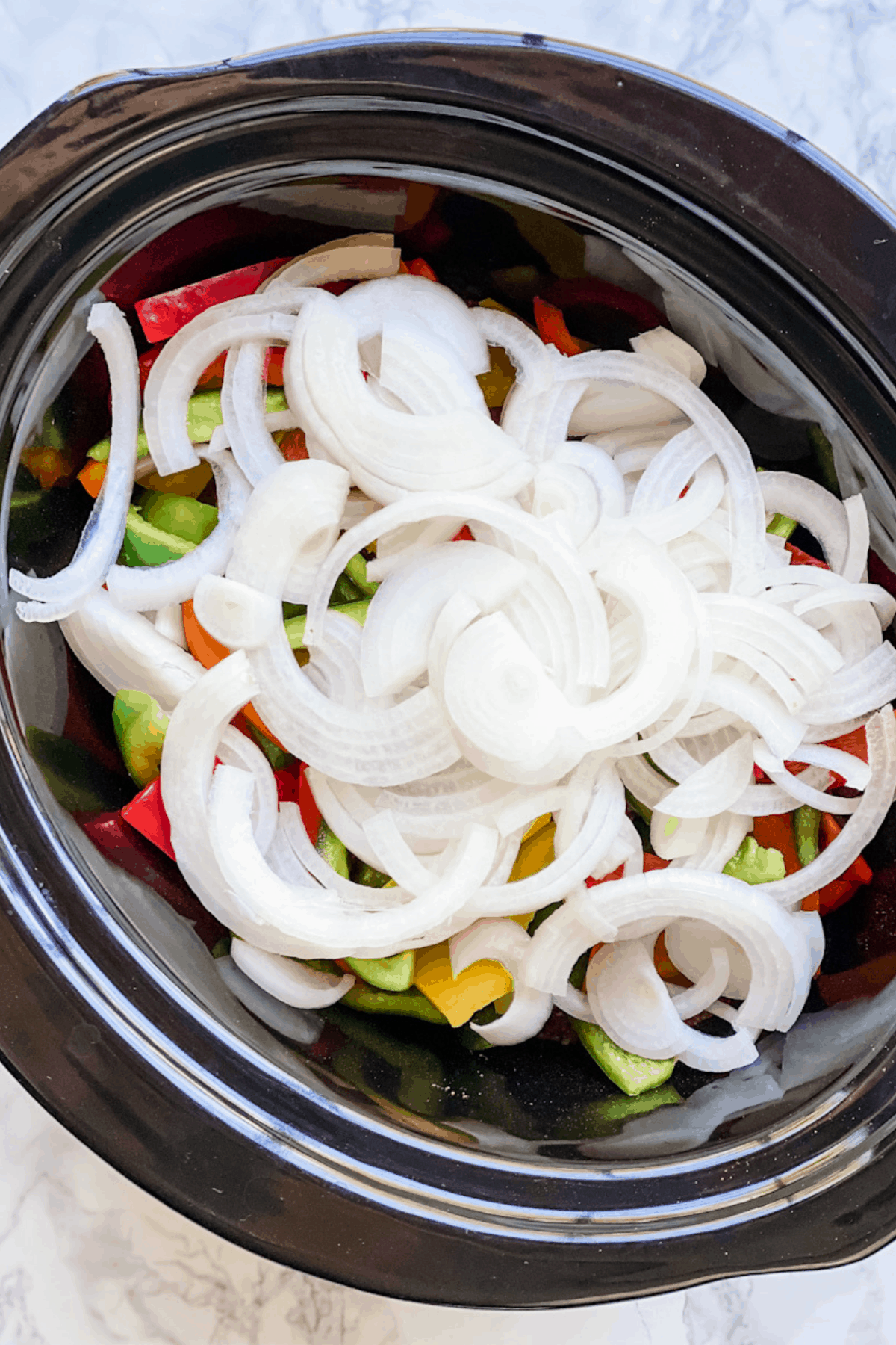Crockpot insert filled with steak, peppers, and onions for fajitas.