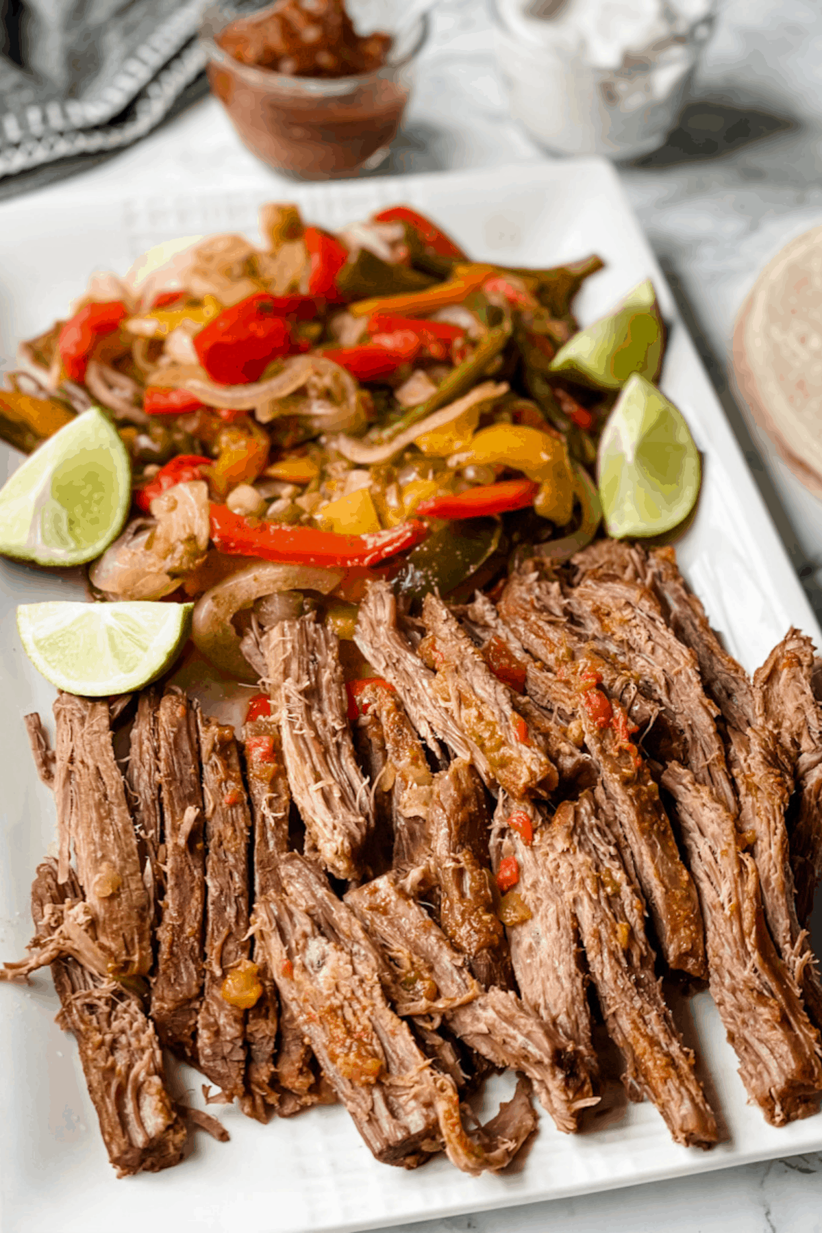 Sliced flank steak to use for fajitas on a white platter with onions and peppers.