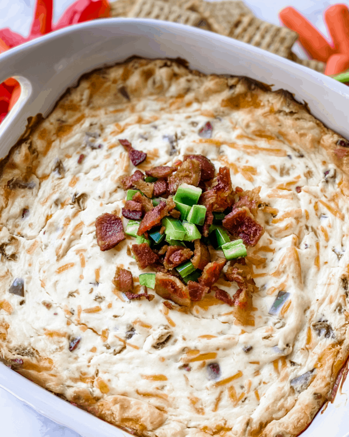 a close up of the cooked jalapeno popper dip with crumbled bacon and jalapeños on top