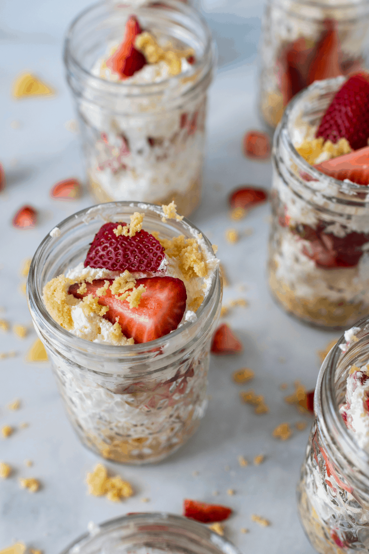 jars of layered strawberry cheesecake and vanilla crumb topping with strawberries on top.