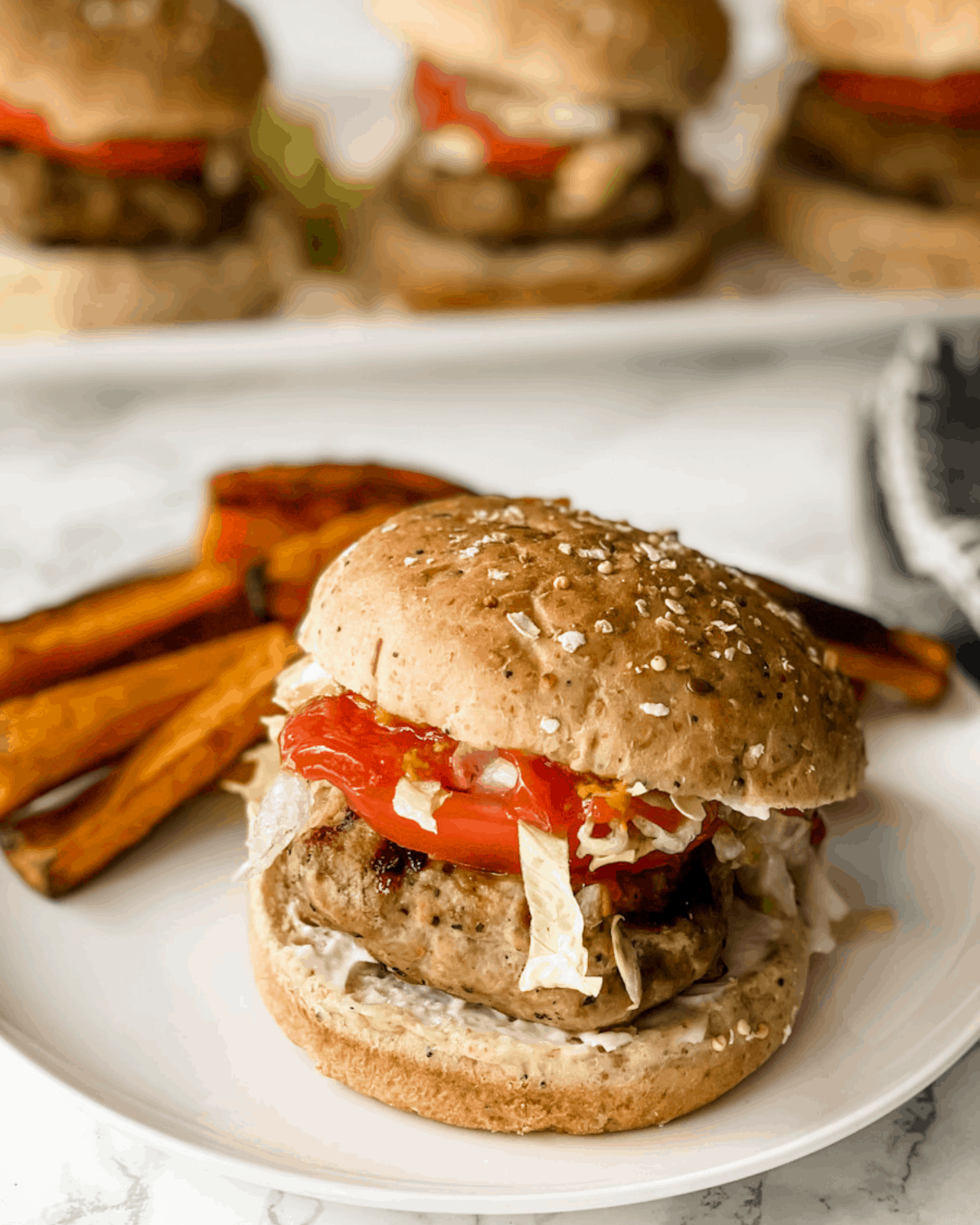 the best turkey burger recipe. A turkey burger on a whole wheat roll with sweet potato fries in the back.