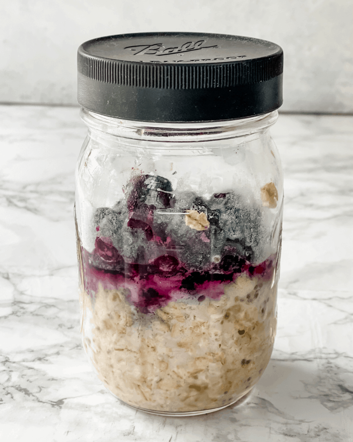 All of the ingredients for overnight oats with blueberries and banana in a jar.