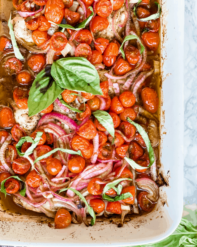 chicken breasts baked in a ceramic dish with tomatoes, red onion, and basil.