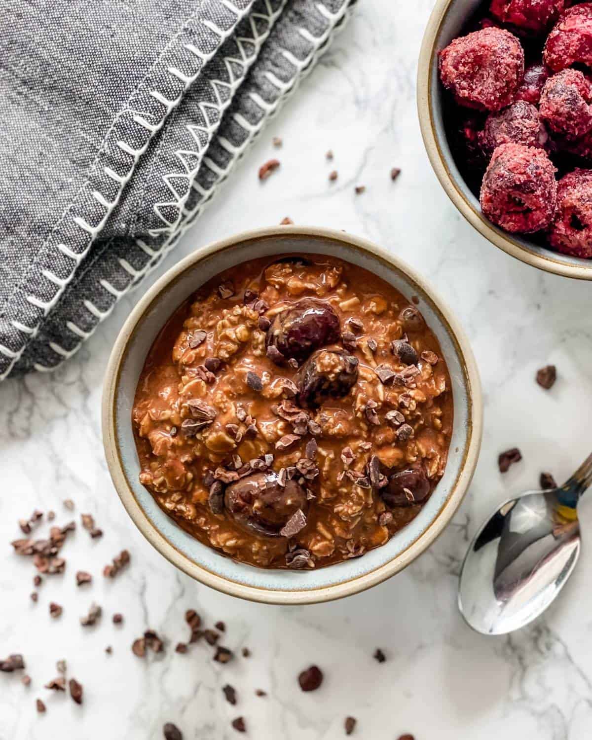 rich chocolate and cherry overnight oats in a bowl with a side of cherries.