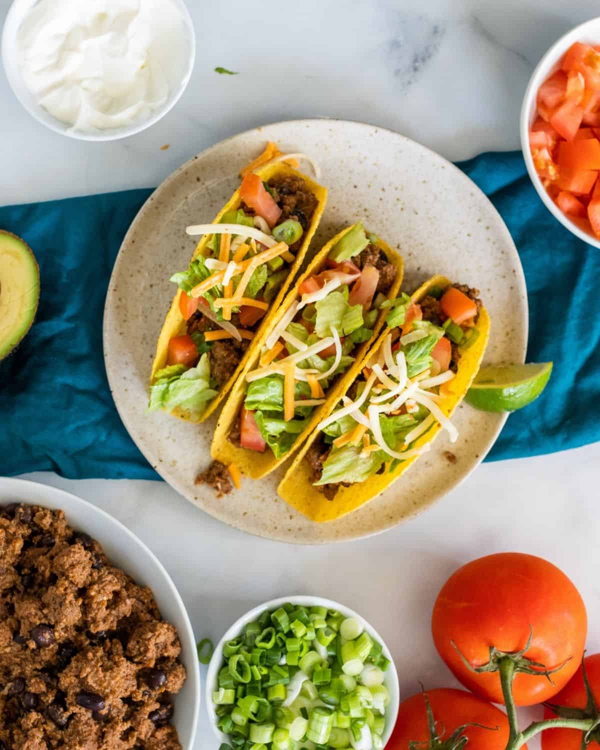 three beef tacos on a plate with condiments around it.